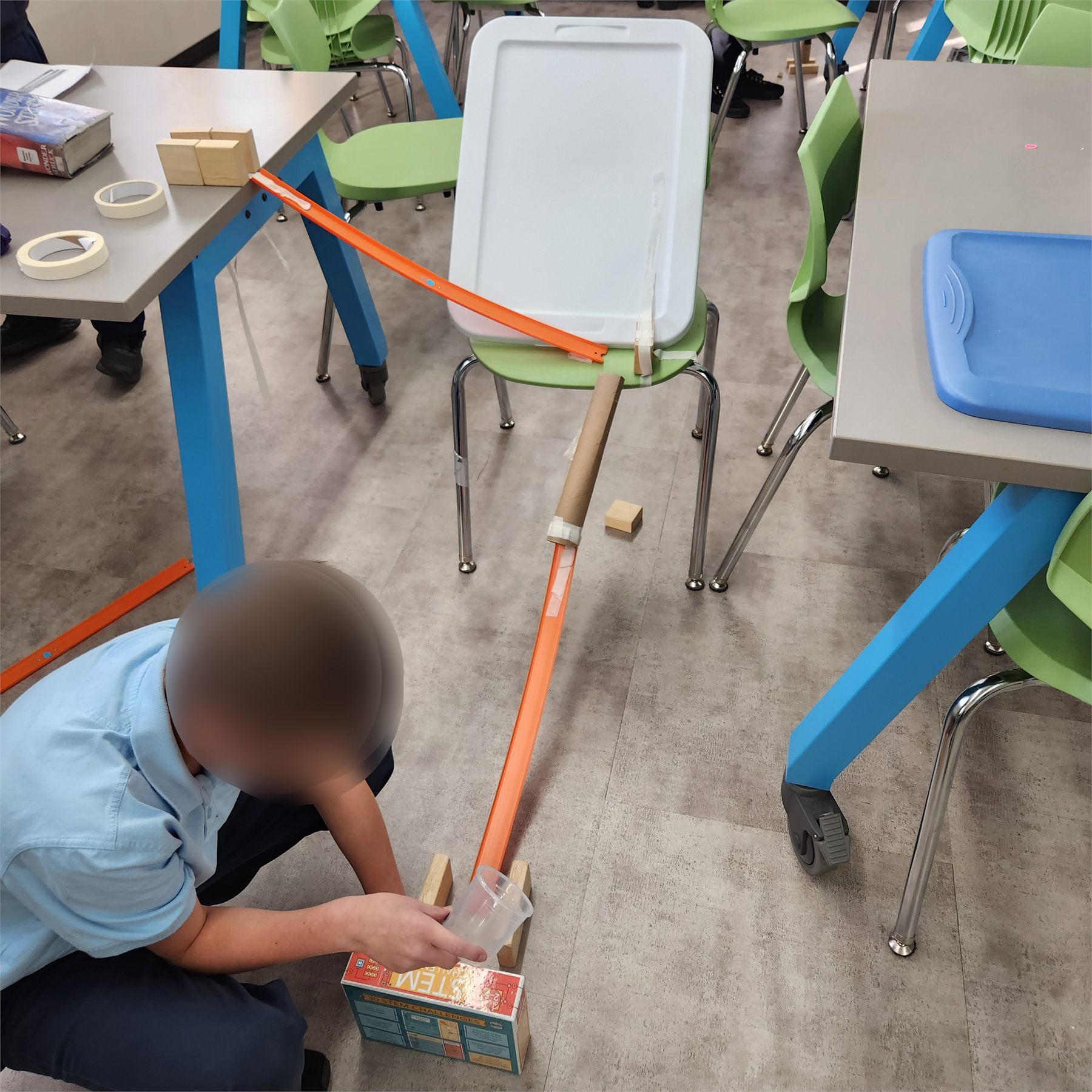 Student testing a Rube Goldberg setup with dominos and ramps